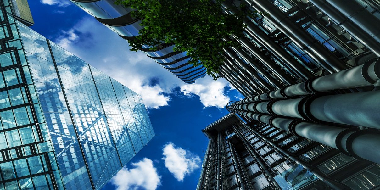Glass office buildings and modern architecture in the City of London, UK. Wideangle image looking up at the towering skyscrapers, with a dazzling blue sky and cloudscape beyond. Taken on a warm sunny day in the capital of England. Horizontal colour image with copy space.